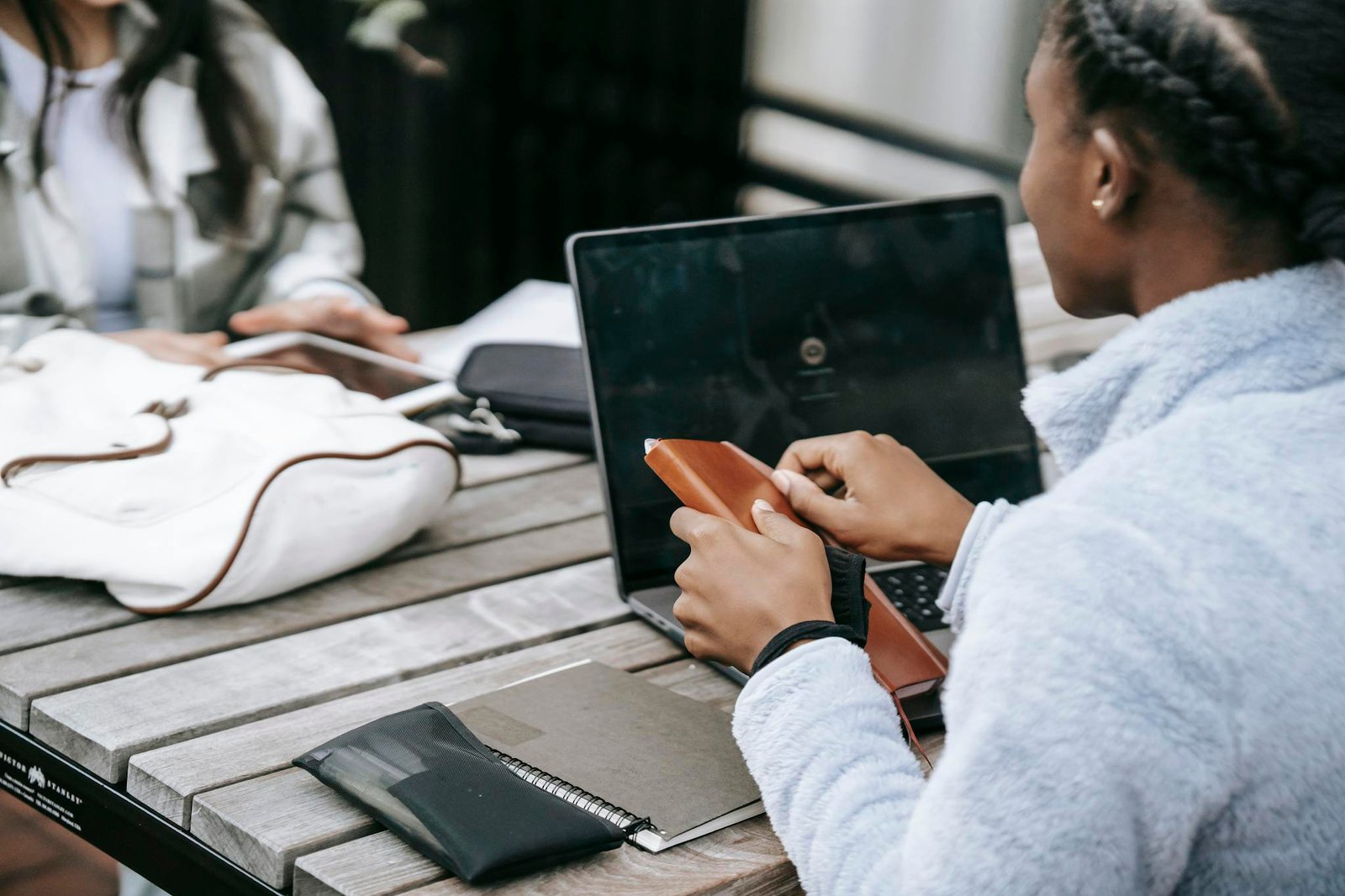 Two young women working together on a laptop outdoors, showcasing teamwork and digital collaboration.